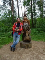 2022.06.19 With a wooden sculpture of an old man, either from the “Tale of the Fisherman and the [Golden] Fish” (its tail is visible below), or from “The Frog Princess” fairy tale (though I do not remember an old man in it) in the “Fairy Tale” Park in Gus-Khrustalny