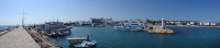 Панорама внешней (на море) набережной бухты айя-напского порта (Λιμανάκι Αγίας Νάπας), самой бухты с кораблями, левым маяком на выходе из неё и Портовым (Λιμανάκι) пляжем вдали.