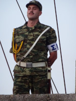 Какой-то военный праздник в Родосе (Ρόδος): строго выправленный военный у флагштока с греческим флагом (Σημαία της Ελλάδας) на крыше здания на центральной улице.