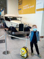 Младший «антикоронавирусный» путешественник по-прежнему поехал с жёлтым чемоданчиком-«пчёлкой», но на этот раз он неожиданно гармонировал по цвету с рекламой такси над старинным автомобилем (который, видимо, использовало это такси).