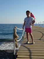 Мой младший сын на пирсе с турецким флагом (Türkiye Cumhuriyeti bayrağı) и Средиземным морем.