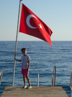 Мой младший сын на пирсе, держась за флагшток большого турецкого флага (Türkiye Cumhuriyeti bayrağı).